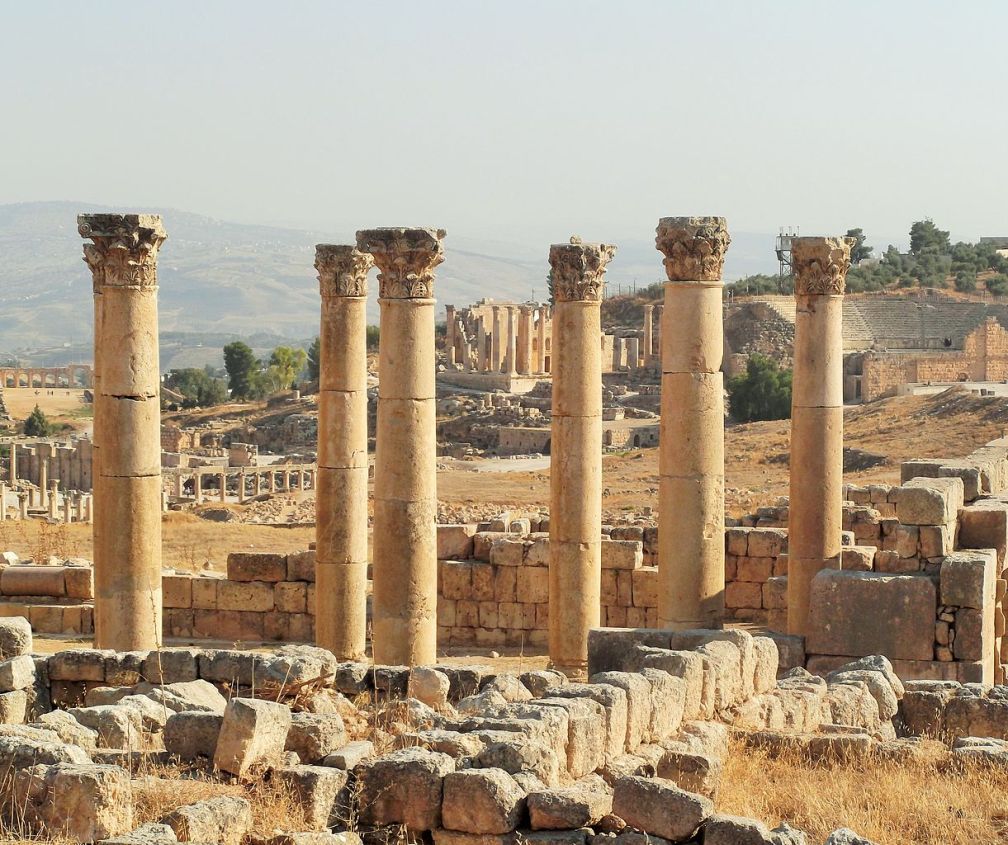 The image is of the ruins of an old city, with dark yellow stone walls and pillars on a hillside. All of the buildings have long crumbled away. The image is of Jerash, a city in Jordan that dates back to 7,000 BCE.