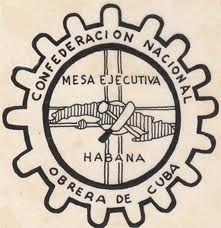 The insignia for the National Workers Confederation of Cuba is the shape of the island of Cuba, with a machete and hammer crossed in front of it, all inside a circular gear with the union's name curved around the gear.